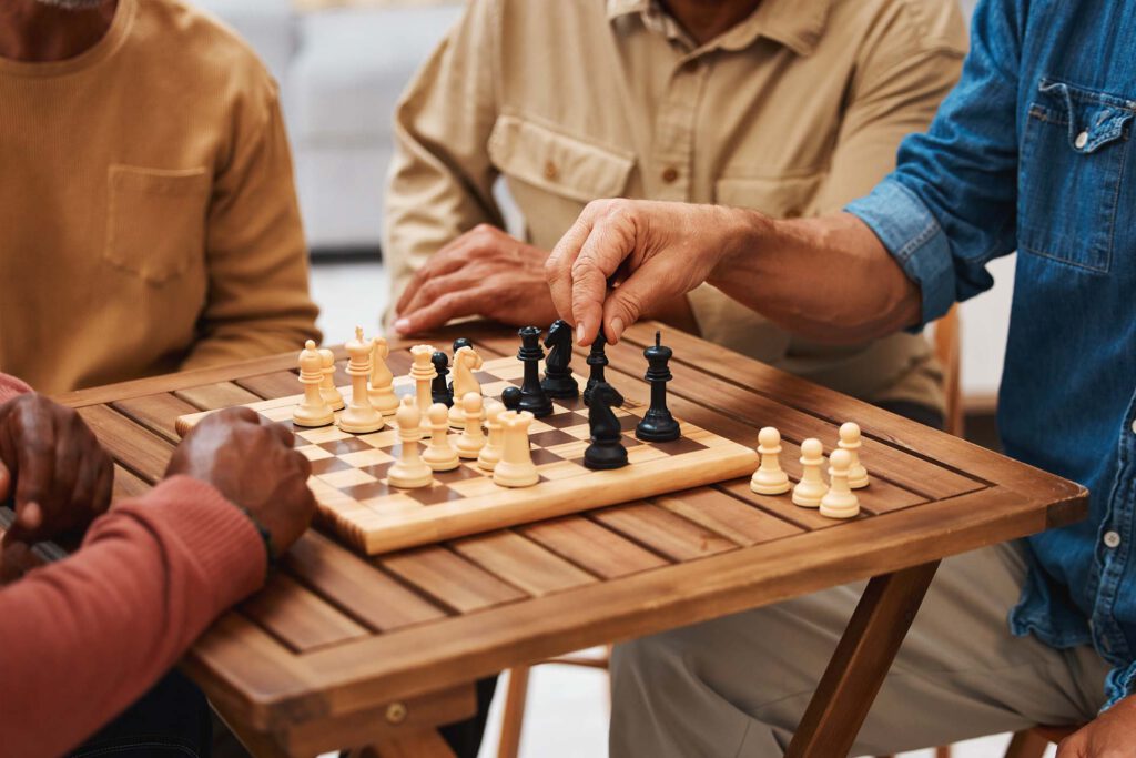 Hands, chess and friends in board games on wooden table for strategic competition, tactical move or.